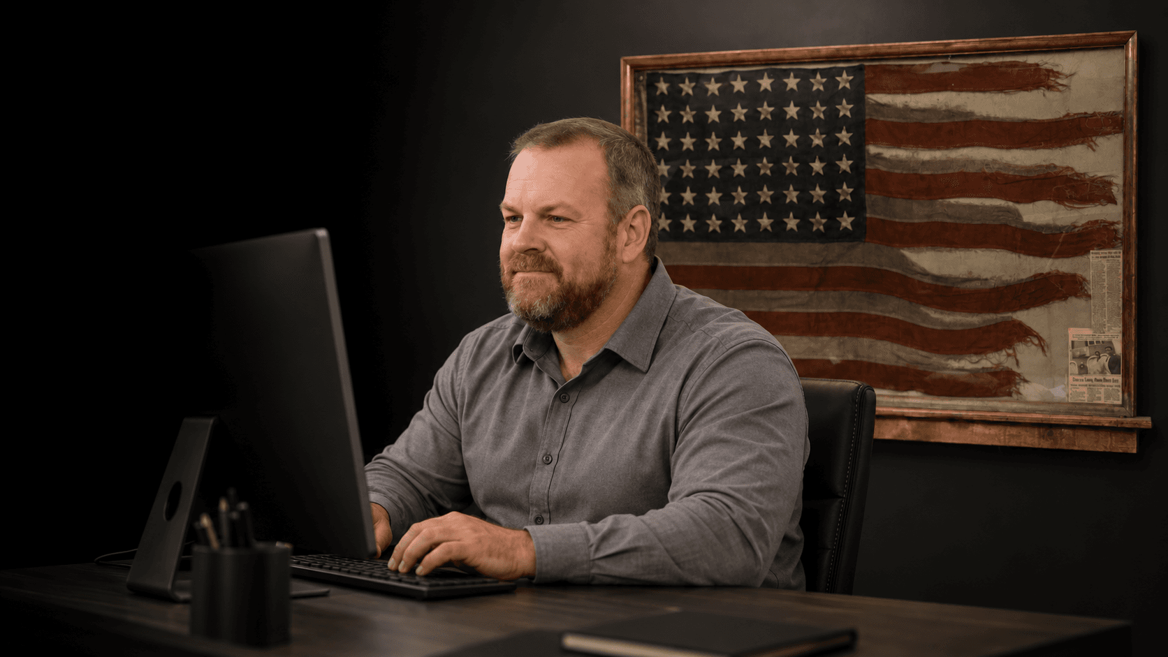 Dave working at his desk, with a framed American flag on the wall behind him